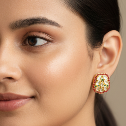 Rounded-rectangle shape with gold-tone metal, multiple tear-drop and round white stones and small green stones in the center, and a border of small red stones